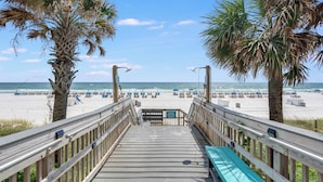 A wooden boardwalk leading to a beach with palm trees, beach chairs, and umbrellas. - Princess Condos - All Units Are Gulf Front & Direct Beach Access in PCB! (Panama City Beach)