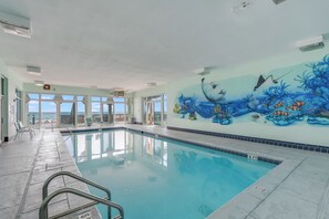 Ein Innenpool mit klarem, blauem Wasser, einer Wandmalerei mit Meereslebewesen und Blick auf den Ozean durch große Fenster.