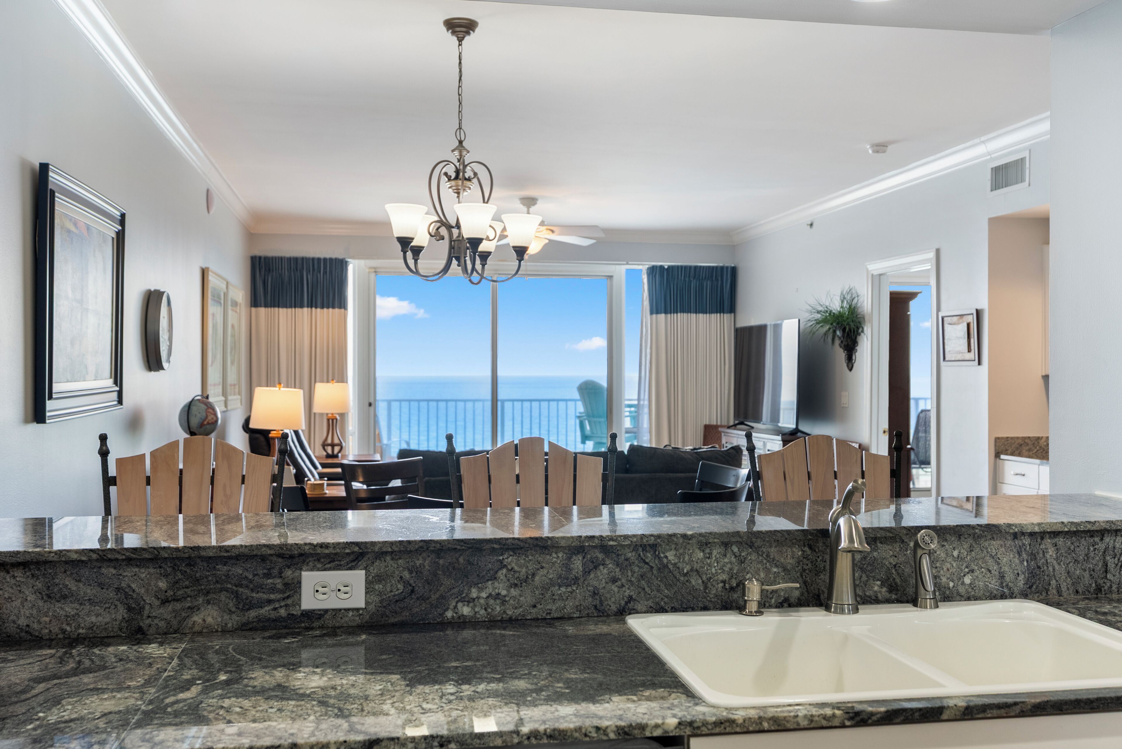 A modern kitchen with a granite countertop, a double sink, and a chandelier.
