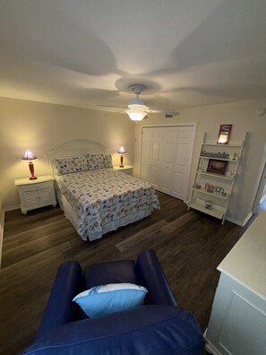 A bedroom with a bed, nightstands, a ceiling fan, a wardrobe, and a shelf with decorative items. - B 11 Sundown Condominiums (Pensacola)