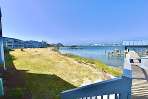 A waterfront property with a grassy lawn, a dock extending into the water, and a building with a blue roof. - B 11 Sundown Condominiums (Pensacola)