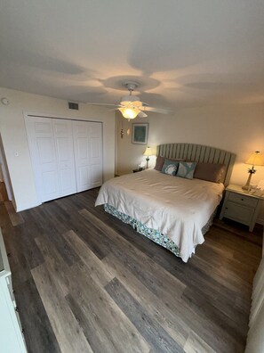 A bedroom with a bed, a ceiling fan, a nightstand, and a door. - B 11 Sundown Condominiums (Pensacola)