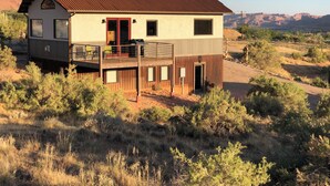 Ein zweistöckiges Haus mit einer Terrasse, umgeben von trockener Vegetation und einer Bergkulisse.