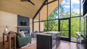 A modern interior with a stone fireplace, wooden ceiling, and large windows offering a view of trees. - The Miller at In the Trees Luxury Resort, Hot Tub, Fireplace, Mountaintop (Hot Springs National Park)