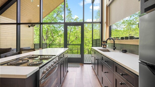 A modern kitchen with a large island, stainless steel appliances, and a view of trees through large windows. - The Miller at In the Trees Luxury Resort, Hot Tub, Fireplace, Mountaintop (Hot Springs National Park)