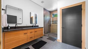 A modern bathroom with a wooden vanity, two mirrors, a shower with a glass door, and a dark door.