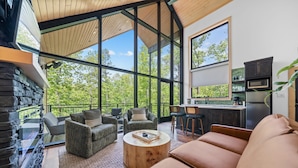 A modern living room with a stone fireplace, large windows, and a kitchen area. - The Eagle at In the Trees, Hot Tub, Mountaintop, Fireplace, Luxury (Hot Springs National Park)