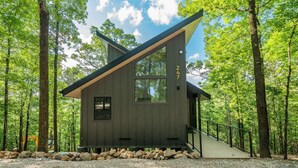 Una cabaña moderna con techo inclinado, ventanas amplias y cimientos de piedra, rodeada por un bosque.