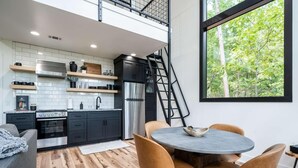 Une cuisine moderne avec un réfrigérateur en acier inoxydable, des meubles de couleur noire et une table à manger en bois, accompagnée de quatre chaises.