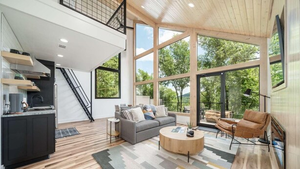A spacious living area with a sofa, coffee table, and a view of the outdoors through large windows. - The Grey Horse at In the Trees Luxury Resort, Mountaintop, Hot Tub, Outdoor Fireplace (Hot Springs National Park)