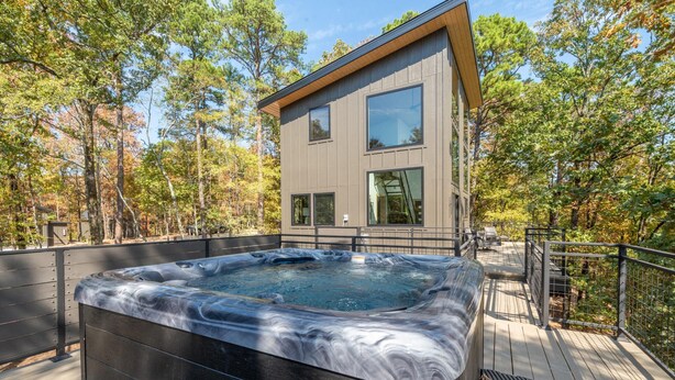 Een modern huis met een jacuzzi op een houten terras, omringd door bomen.