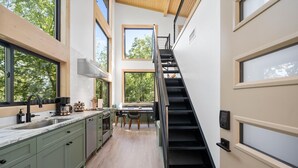 Une cuisine moderne dotée d’un îlot central, d’un coin repas avec une table et des chaises, et d’un escalier noir menant à un niveau supérieur.