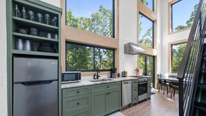 Une cuisine moderne avec des meubles de couleur verte, des appareils en acier inoxydable et de grandes fenêtres donnant sur la verdure.
