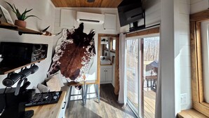 A modern kitchen with a wooden ceiling, a ceiling fan, a mounted TV, and a large cowhide on the wall. - The Fox Den - Peaceful Tiny Home Retreat in the Mountains w/ Hot Tub & Fire Pit (Canton)