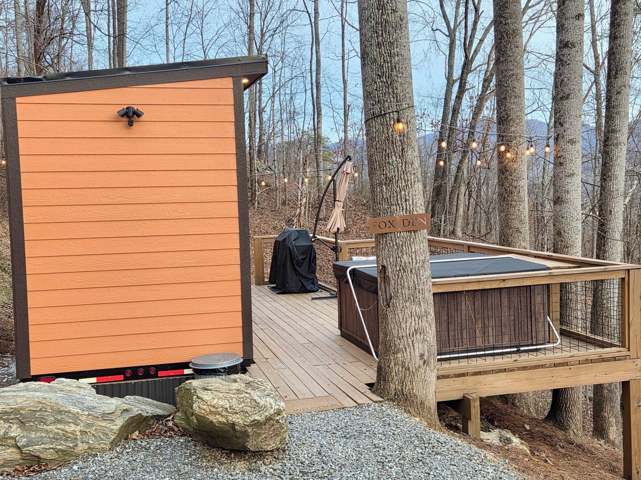 A wooden deck with a hot tub, a barbecue grill, and a small cabin-like structure.