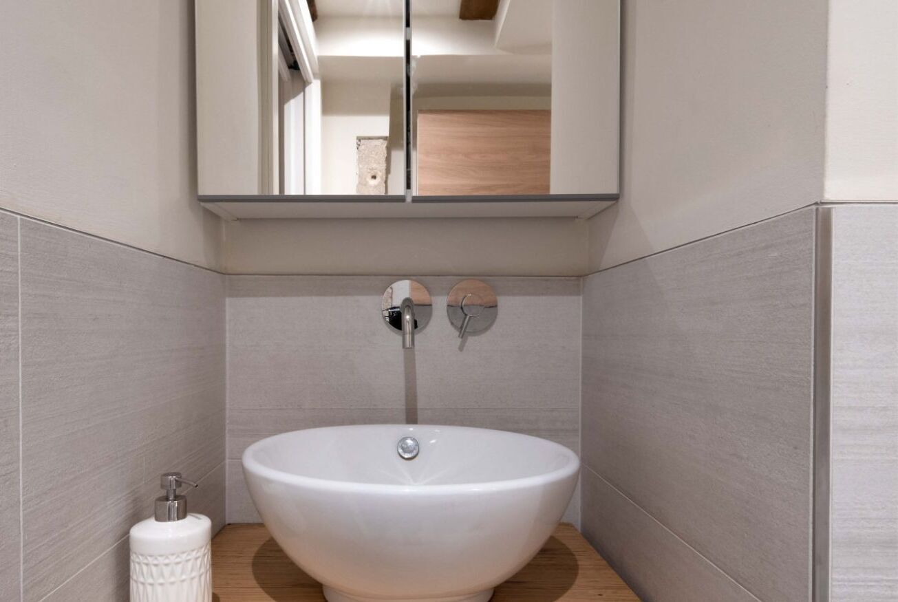 Een moderne badkamer met een wit wastafelmeubel, een spiegel erboven en een zeepdispenser aan de linkerkant.