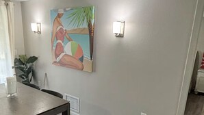 A dining area with a wooden table and chairs, a painting on the wall, and a plant. - Path to Paradise. (Englewood)