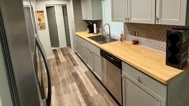 A modern kitchen with grey cabinets, a wooden countertop, stainless steel appliances, and a tiled backsplash. - Path to Paradise. (Englewood)