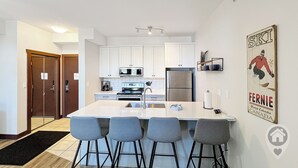 A modern kitchen with white cabinets, a stainless steel refrigerator, and a central island with bar stools. - Top-Floor Silver Rock 1BR – Comfort in Every Stay (Fernie)