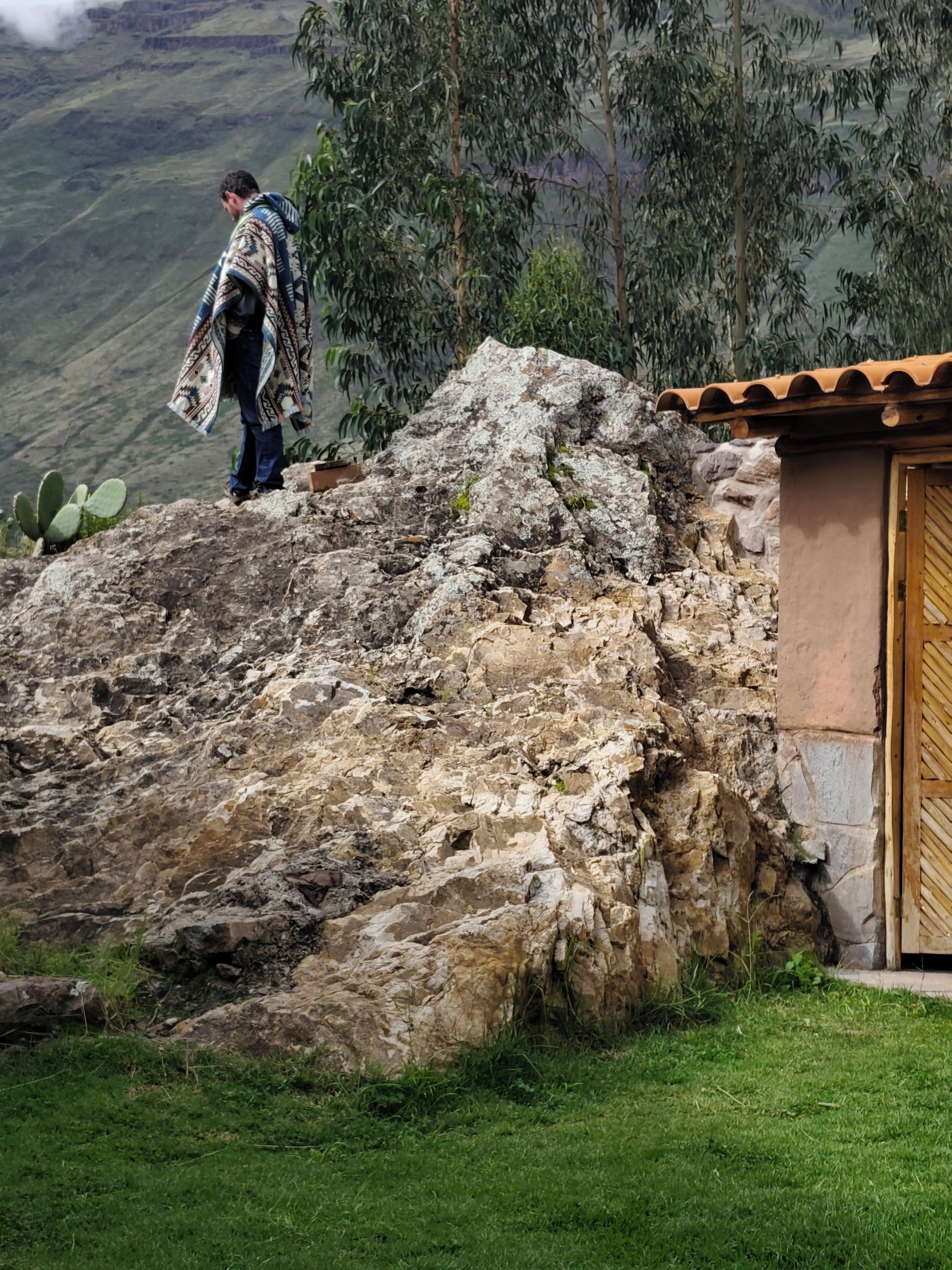 A person standing on a rocky outcrop with a building in the background.