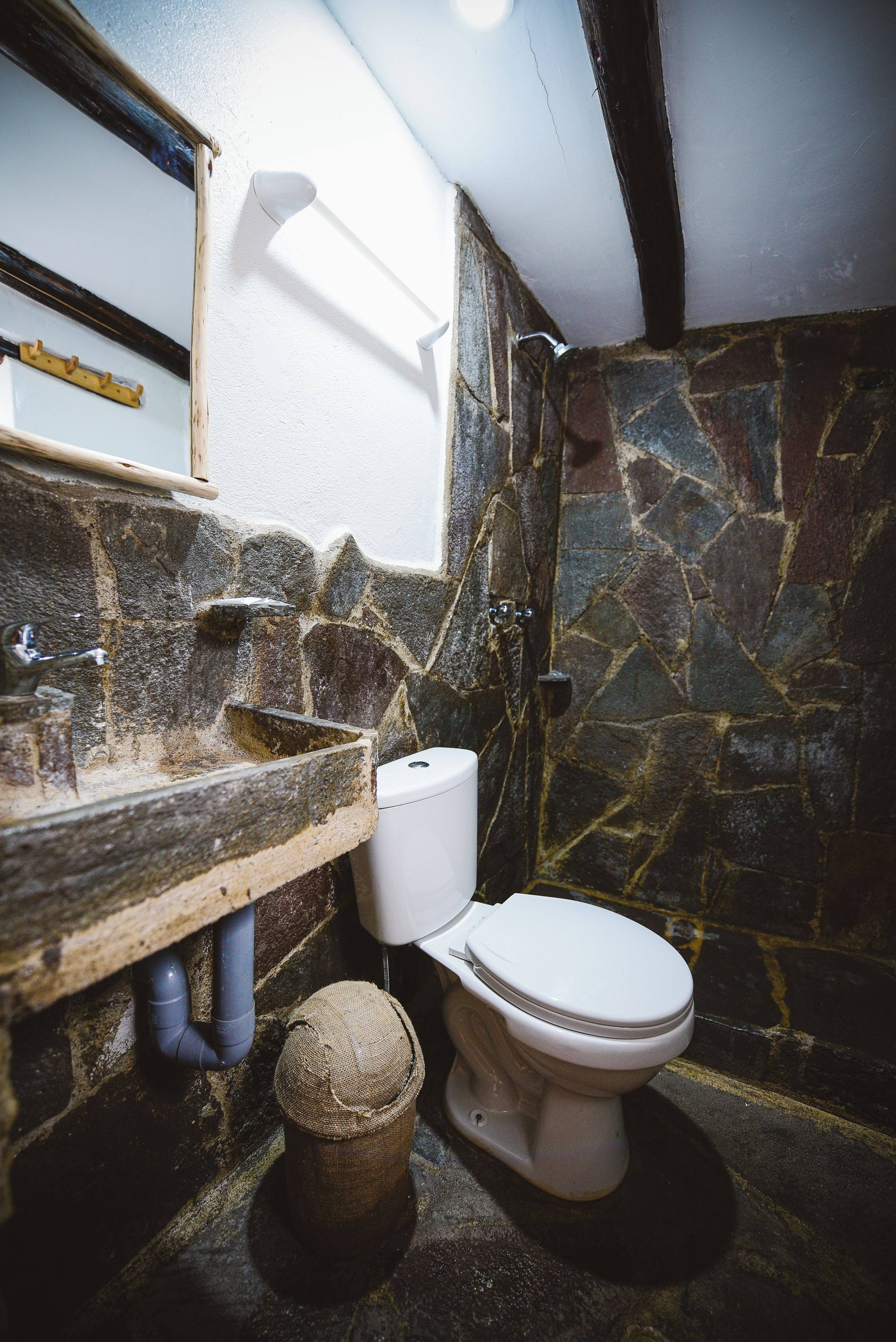 Ein Badezimmer mit einer Steinwand, einer weißen Toilette und einem hölzernen Waschtisch.