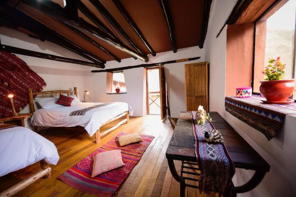 A cozy room with wooden beams, a bed, a bench, and a window with a view.