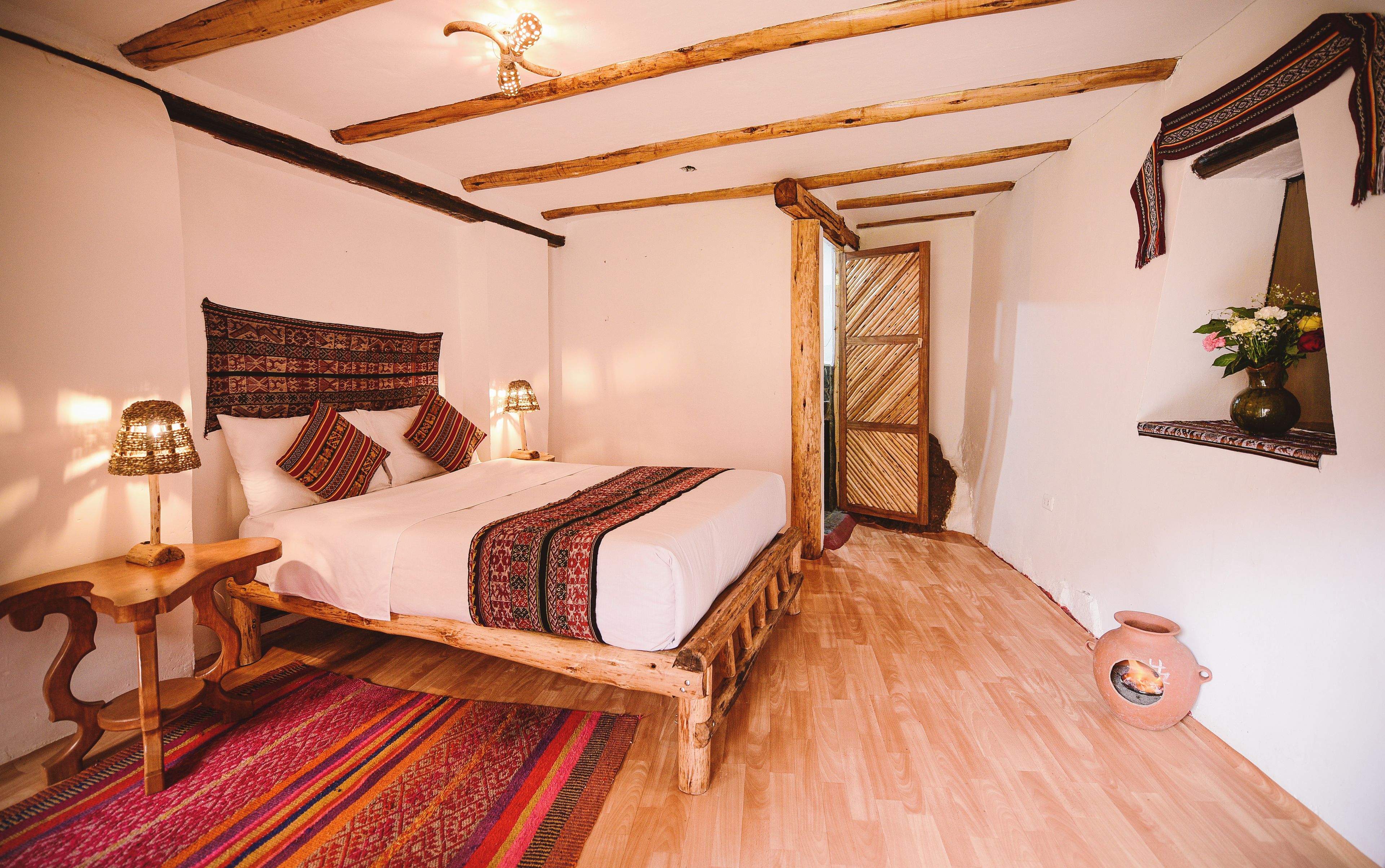 Una habitación con una cama de madera, un tapete tejido, un tapiz en la pared y una lámpara tradicional.