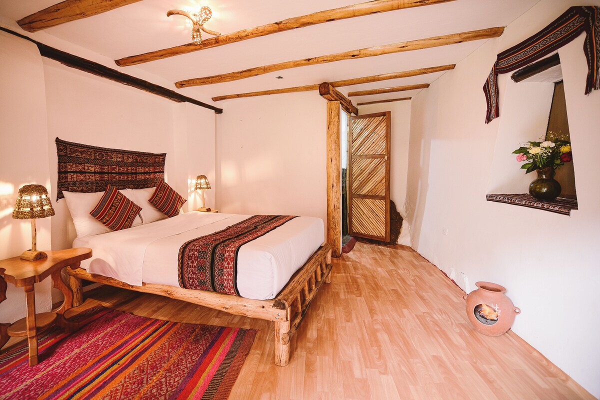 Una habitación con una cama de madera, un tapete tejido, un tapiz en la pared y una lámpara tradicional.