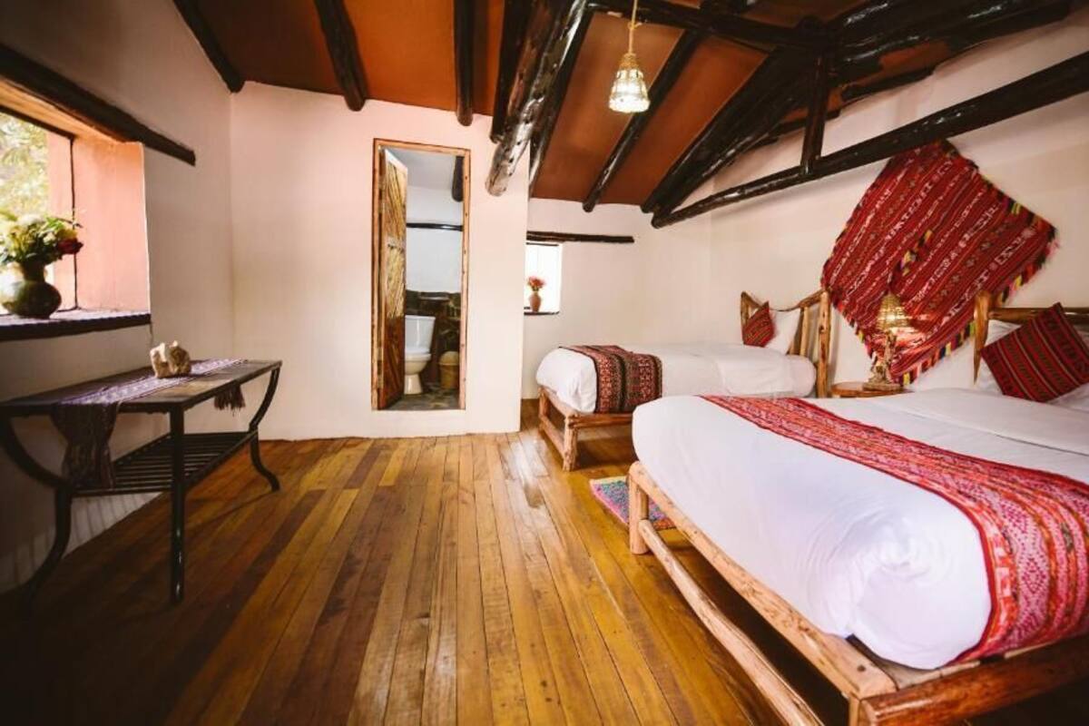 A traditional room with wooden floors, a large bed with red and white bedding, a wooden headboard, a small table with a vase, and a mirror on the wall.