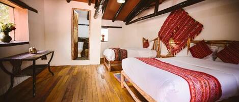 A traditional room with wooden floors, a large bed with red and white bedding, a wooden headboard, a small table with a vase, and a mirror on the wall.
