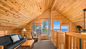Ein gemütliches Cabin-Interieur mit Holzboden, einer Couch, einem Tisch und Meerblick durch große Fenster.