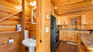 Ein Holzblockhaus-Interieur mit Küchenzeile, einschließlich Spüle, Kühlschrank und Holzschränken.