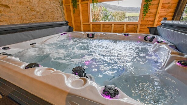 A hot tub with multiple jets, surrounded by wooden walls and a window with a view of greenery. - Le Clos Embelli - ROUVRES LES VIGNES (ROUVRES LES VIGNES)