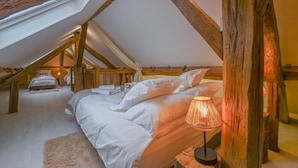 A cozy attic bedroom with a sloped ceiling, a bed with white linens, and a lamp on a wooden nightstand. - Le Clos Embelli - ROUVRES LES VIGNES (ROUVRES LES VIGNES)