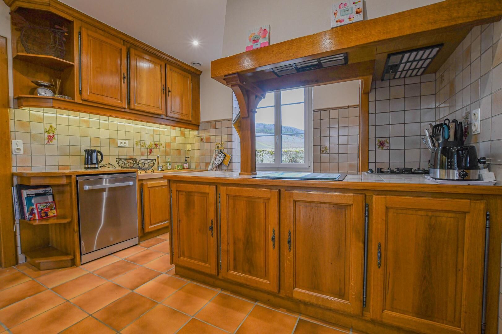 A kitchen with wooden cabinets, a dishwasher, a window, and a tiled backsplash.
