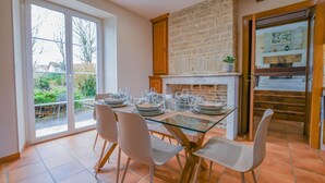 A dining area with a glass table, white chairs, and a brick wall. - Le Clos Embelli - ROUVRES LES VIGNES (ROUVRES LES VIGNES)