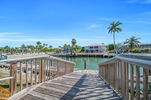 A wooden boardwalk leading to a marina with boats, palm trees, and a building with a white roof. - 7026 Waterfront Duck Key Villa - Sleeps 6 (Marathon)