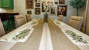 A dining room with a long table, chairs, a chandelier, and framed pictures on the walls.