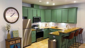 Una cocina moderna con armarios verdes, electrodomésticos de acero inoxidable, un reloj y una zona de bar con taburetes.