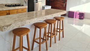 Eine moderne Küche mit Marmor-Spritzschutz, einem eingebauten Gasherd, einem Edelstahl-Kühlschrank und Holzbarhocker.