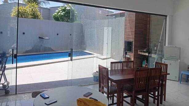 Eine moderne Terrasse mit Glastür zum Schwimmbecken, einem Esstisch mit Stühlen und einer kleinen Küchenzeile.