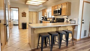 A kitchen with wooden cabinets, a central island with stools, a microwave, and a 'Wi-Fi' sign. - Wild Aspen Ridge | Space to Gather, Room to Unwind (Heber-Overgaard)