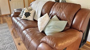 A brown leather sofa with multiple cushions in a room with wooden flooring and a door in the background. - Wild Aspen Ridge | Space to Gather, Room to Unwind (Heber-Overgaard)