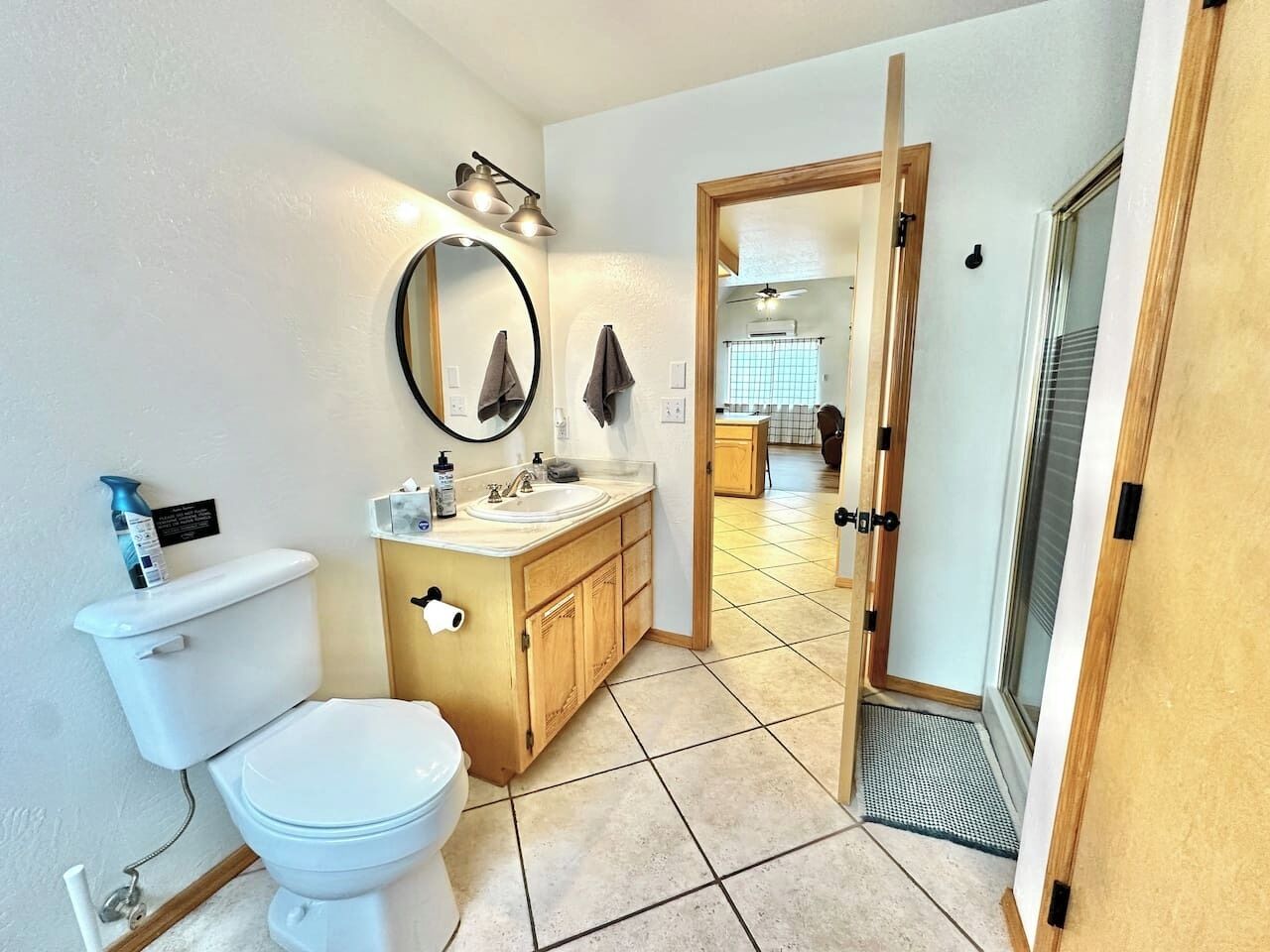 Een kleine badkamer met toilet, wastafel en spiegel, aansluitend aan een keuken.