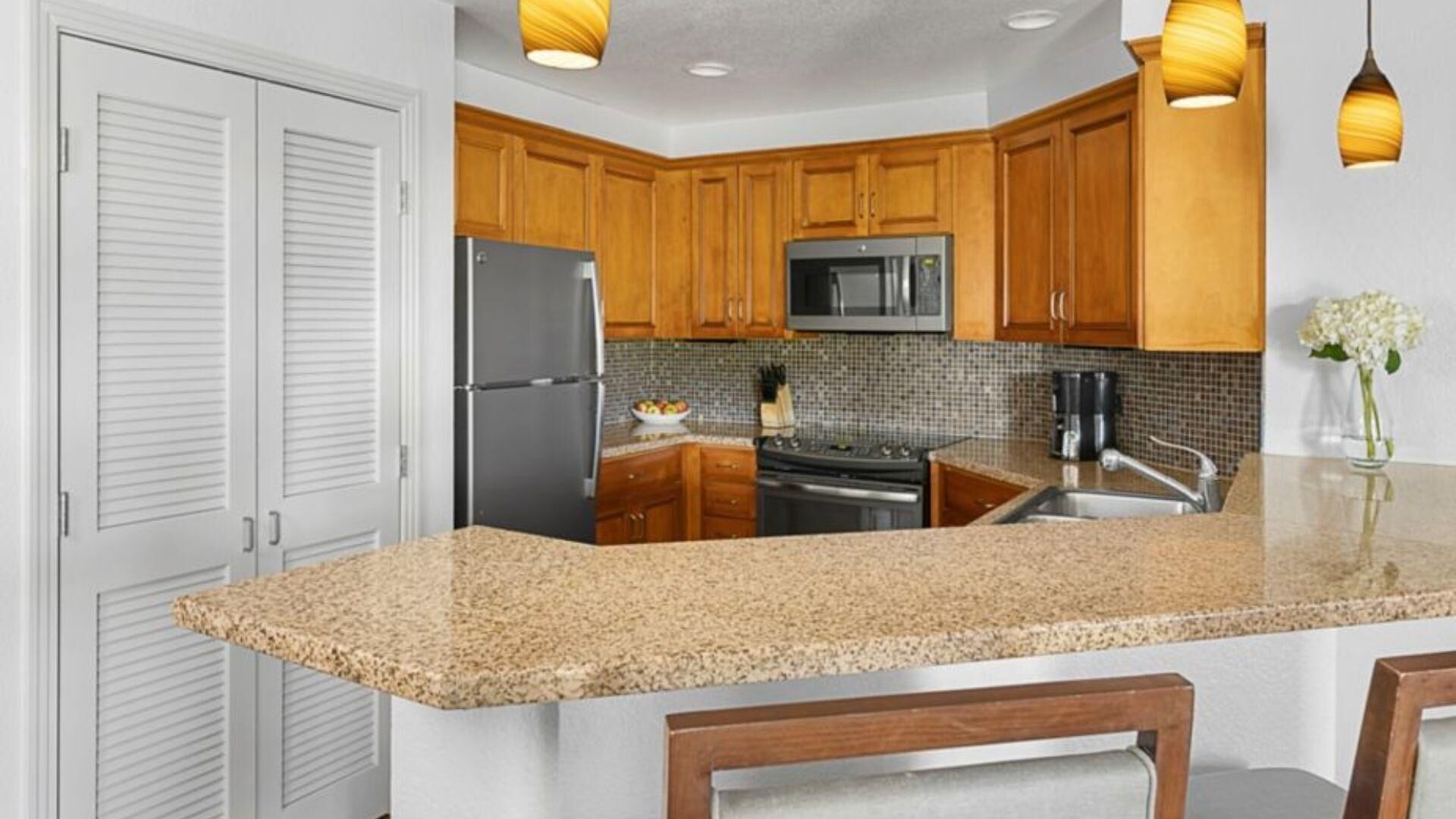 Una cocina con armarios de madera, electrodomésticos de acero inoxidable, encimera de granito e iluminación colgante.