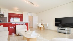 A modern living room with a sofa, a coffee table, a TV, and a dining area with chairs and a table. - Le Maria - 2 bedroom - 2 Bath - Terrace (Cannes)