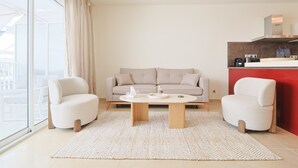 A modern living room with a sofa, two armchairs, a coffee table, and a kitchen area with a red accent wall. - Le Maria - 2 bedroom - 2 Bath - Terrace (Cannes)