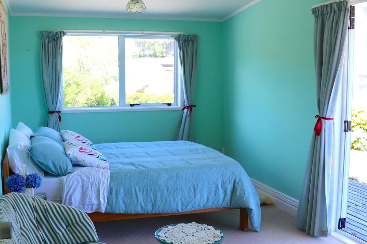 A bedroom with a bed, a chair, a small table, and a window with curtains.