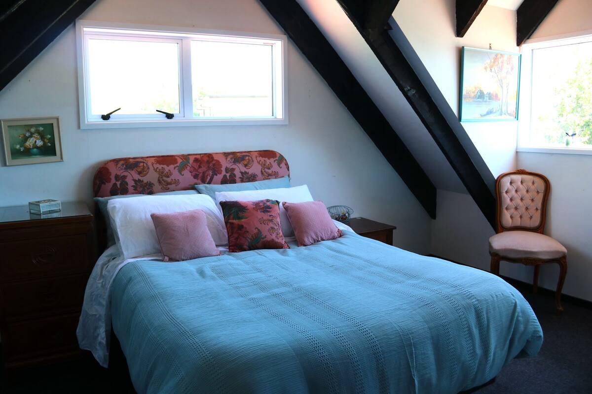 A bedroom with a bed, a nightstand, a chair, and two windows.