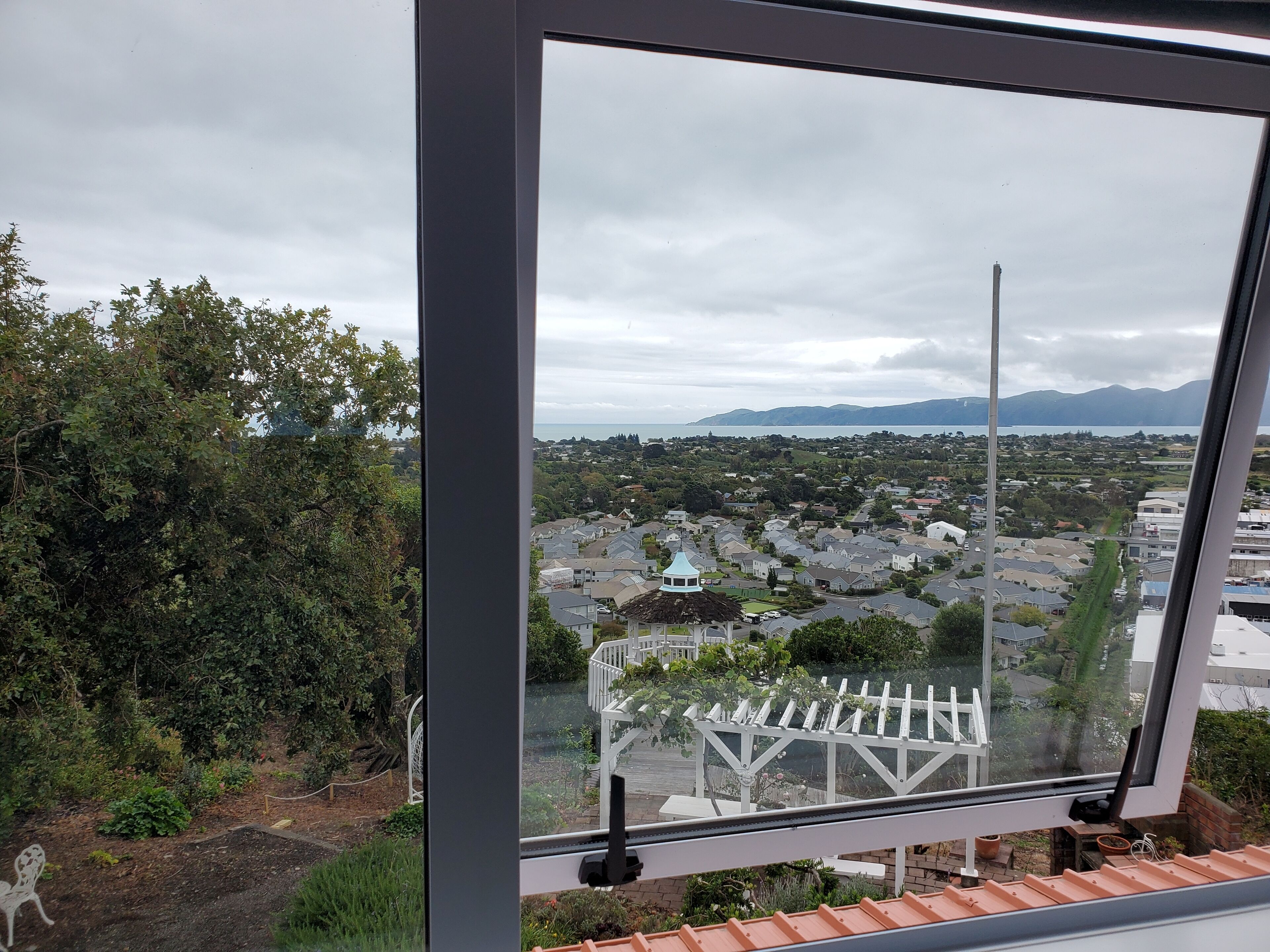 A view from a window overlooking a residential area with houses, a gazebo, and mountains in the distance.